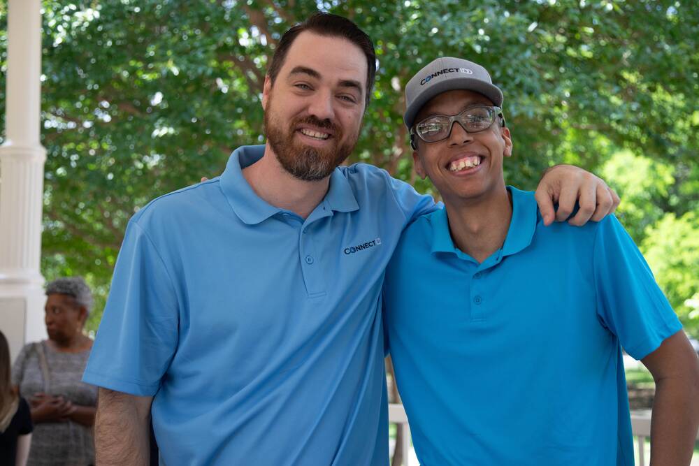Two men in blue ConnectIDD polos smile with their arms around each other.